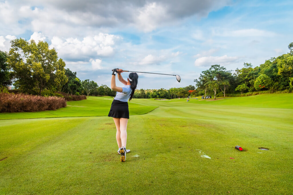 A woman holds her finish and watches the ball after taking a shallow golf swing