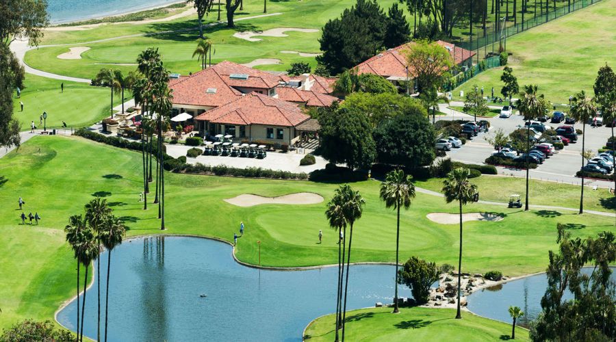 A stunning view of one of the best golf courses in San Diego, featuring lush fairways, a serene lake, palm trees, and a vibrant blue sky.