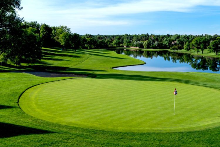 A well-maintained green overlooking a serene lake and lush surroundings at Cherry Hills Country Club, a premier golfing destination in Denver.