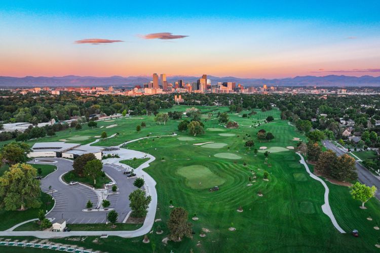 An aerial view of City Park Golf Course at sunset, featuring sprawling greens, a clubhouse.