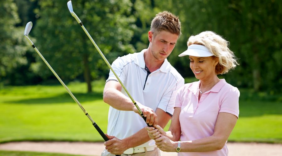 A golf instructor teaching a woman the proper golf grip on a sunny course.