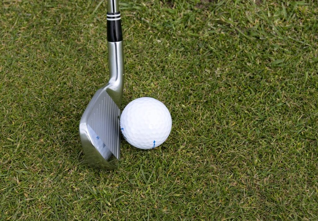 A golf iron positioned beside a ball on the fairway grass, ready for an approach shot